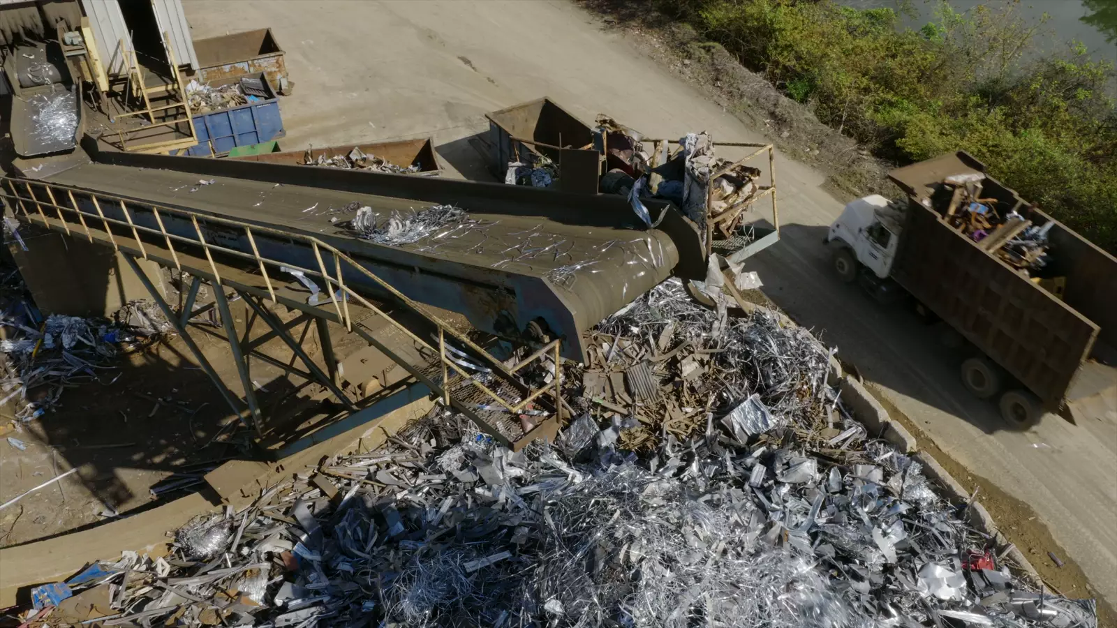 Scrap metal yard seen from above, with a conveyor belt and a loaded truck